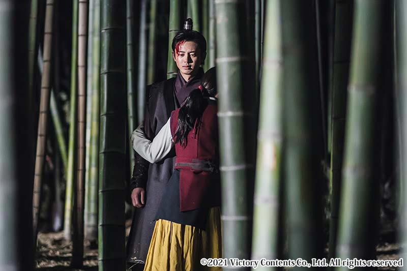 竹藪の中で血を流す男性を抱きしめる女性