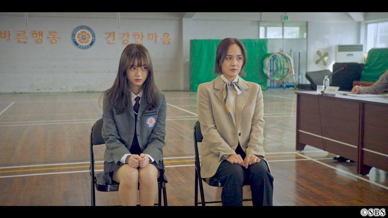 椅子に座る女性と女子学生